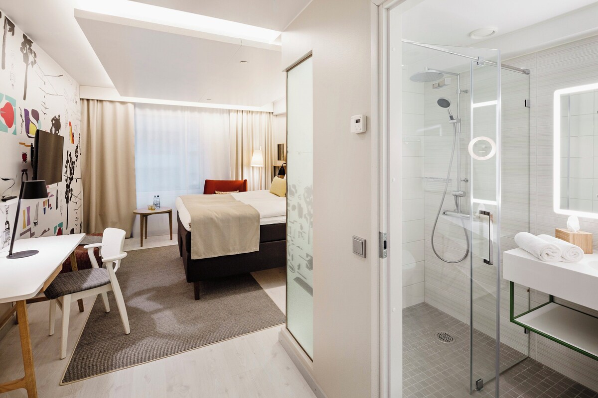 Ein Hotelzimmer mit Bett, Schreibtisch, Stuhl und Dusche.