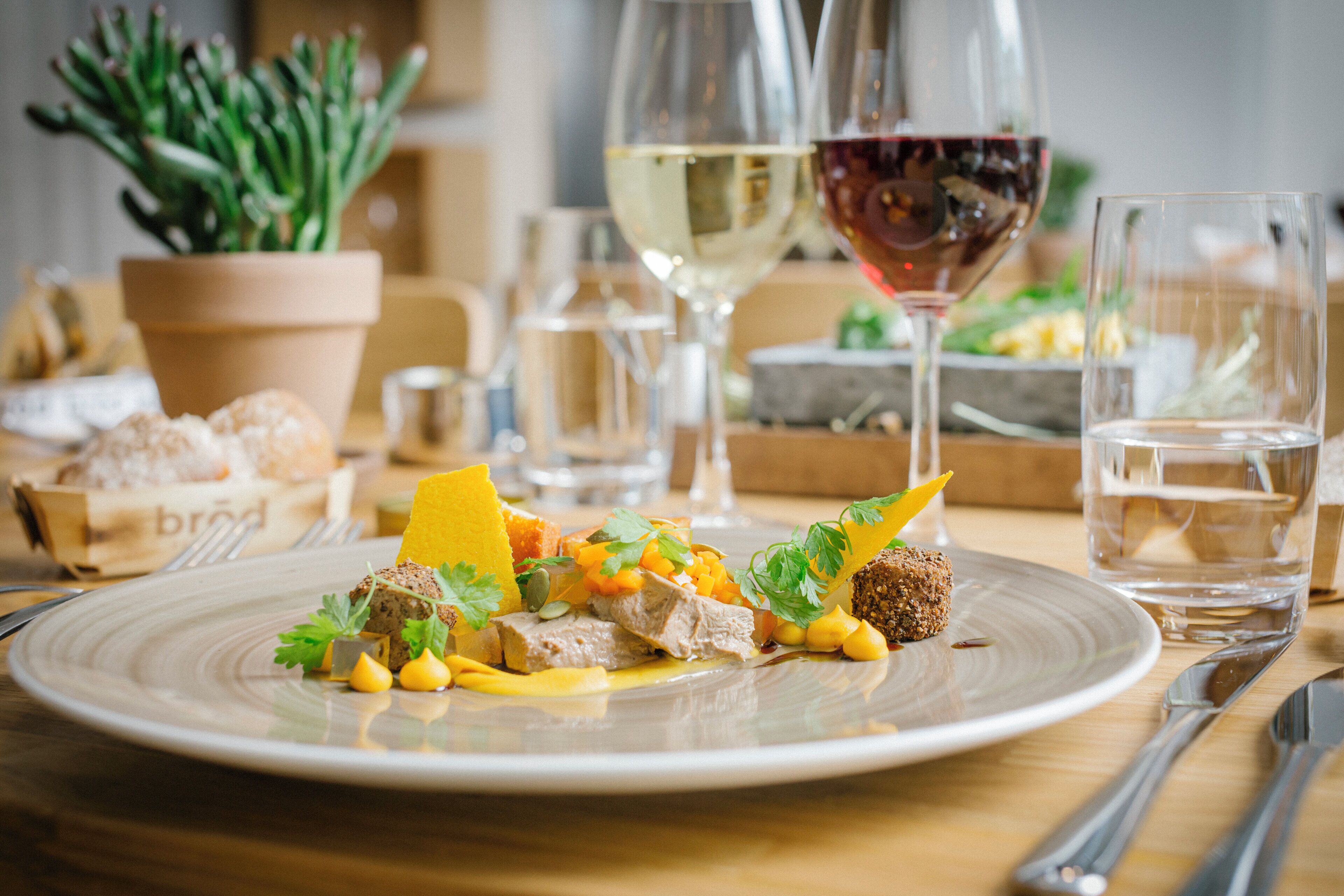 Una mesa de comedor con un plato de comida, copas de vino y una planta en maceta.
