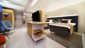 Une chambre d’hôtel moderne équipée d’un lit, d’un bureau avec un téléviseur à écran plat, d’une chaise et d’une petite table.