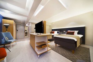 A modern hotel room with a bed, a desk with a flat-screen TV, a chair, and a small table. - Hotel Indigo Helsinki - Boulevard by IHG (Helsinki)