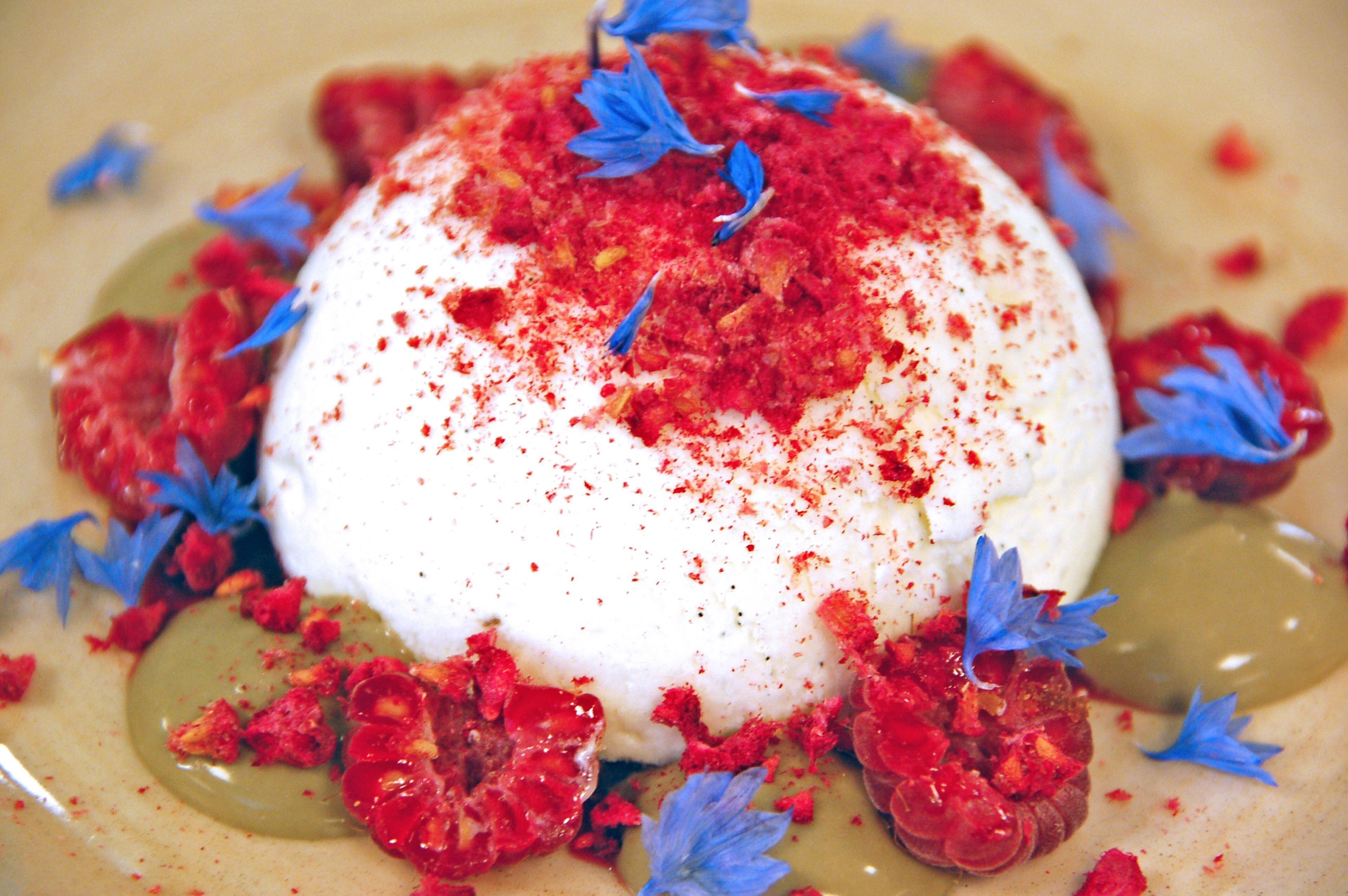 Un postre con base blanca, cobertura roja y flores comestibles azules.