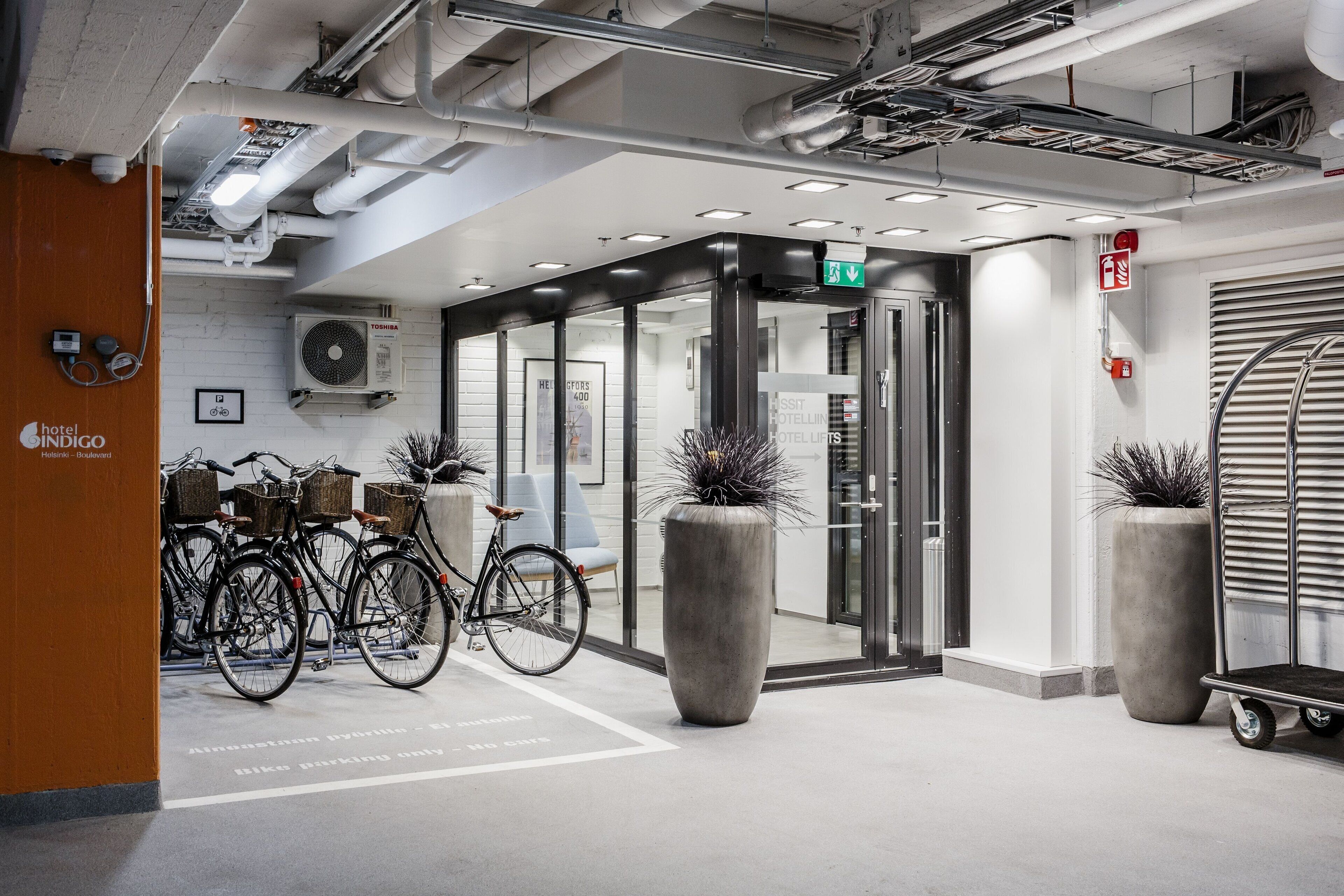 A hotel entrance with a bike parking area, a turnstile, and a sign for hotel lifts.