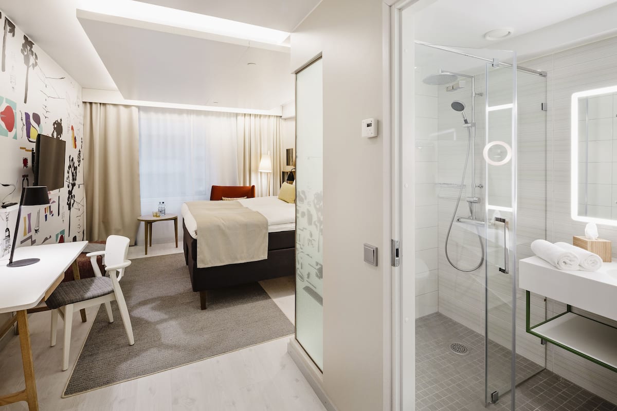 A hotel room with a bed, desk, chair, and a shower area.