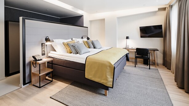 Une chambre d’hôtel moderne équipée d’un lit, d’une table de chevet, d’une lampe et d’un téléviseur fixé au mur.