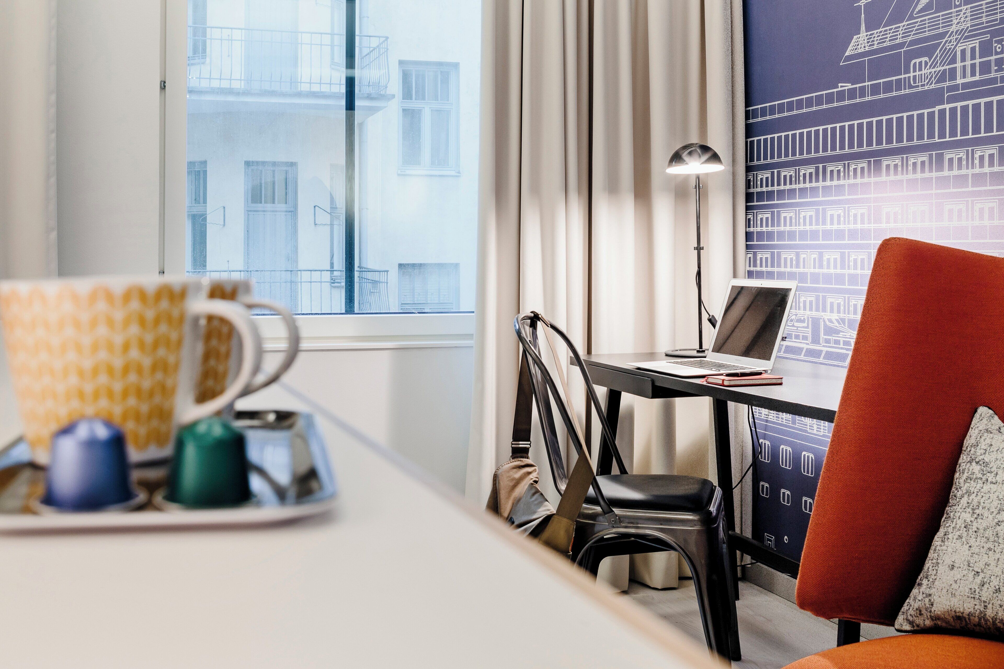 A hotel room with a desk, chair, and a view of buildings through the window.