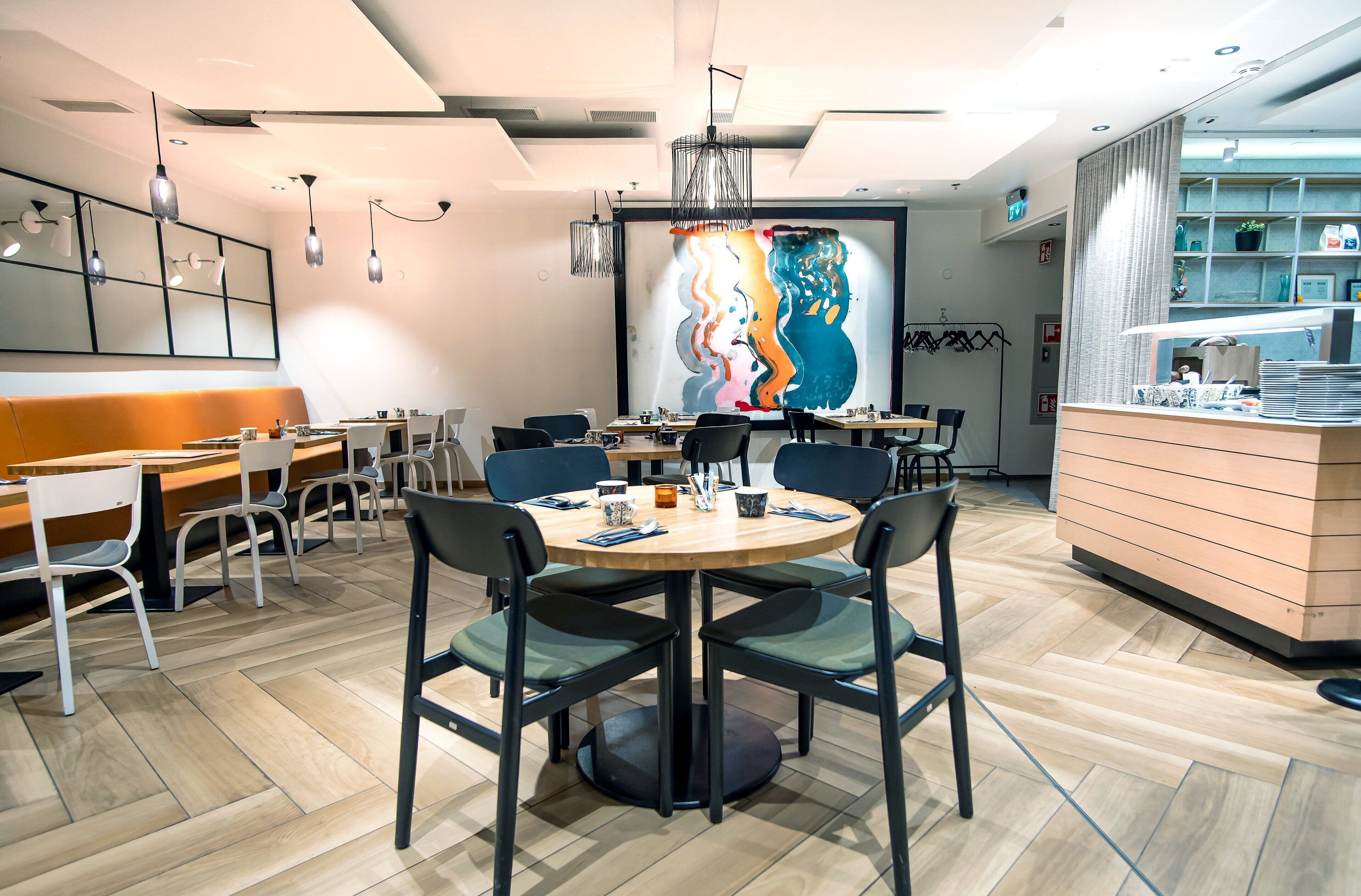 A modern dining area with round tables, black chairs, and a large abstract painting on the wall.