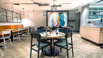A modern dining area with round tables, black chairs, and a large abstract painting on the wall.