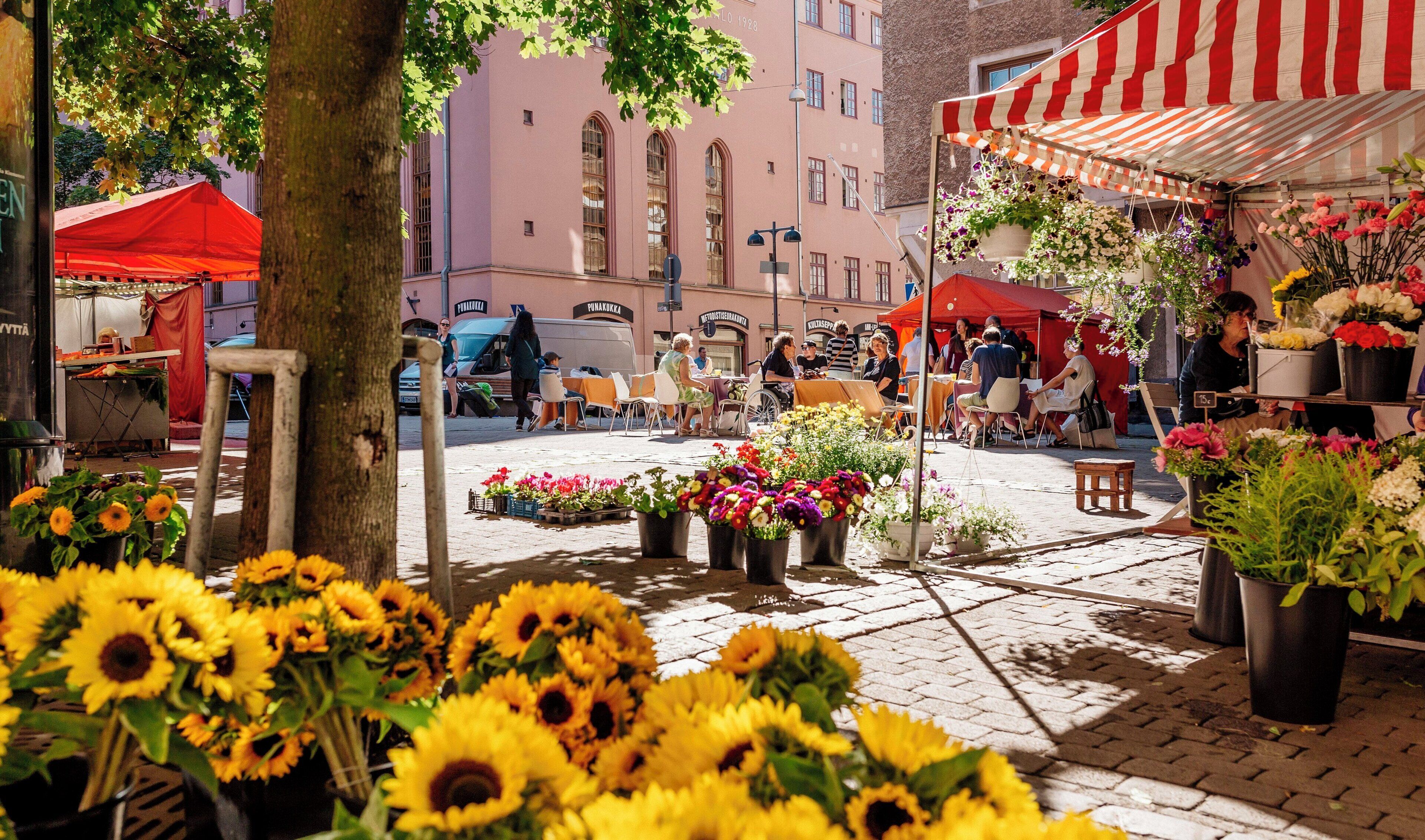 Un mercado al aire libre con varios puestos, incluyendo un puesto de flores con girasoles y otras flores.