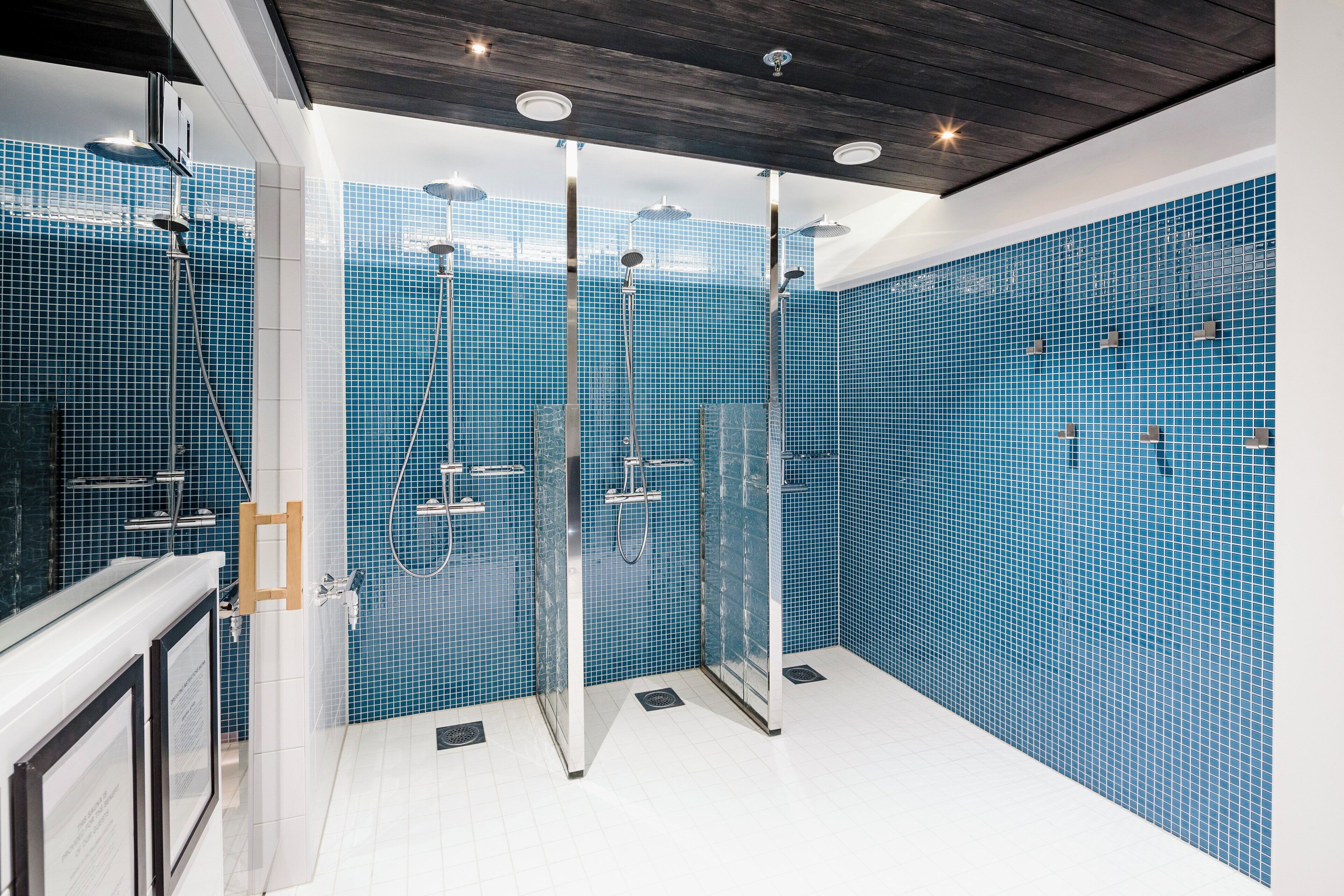 Un baño moderno con paredes de azulejos azules, cabina de ducha con mampara de vidrio y techo de madera.
