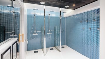 Un baño moderno con paredes de azulejos azules, cabina de ducha con mampara de vidrio y techo de madera.