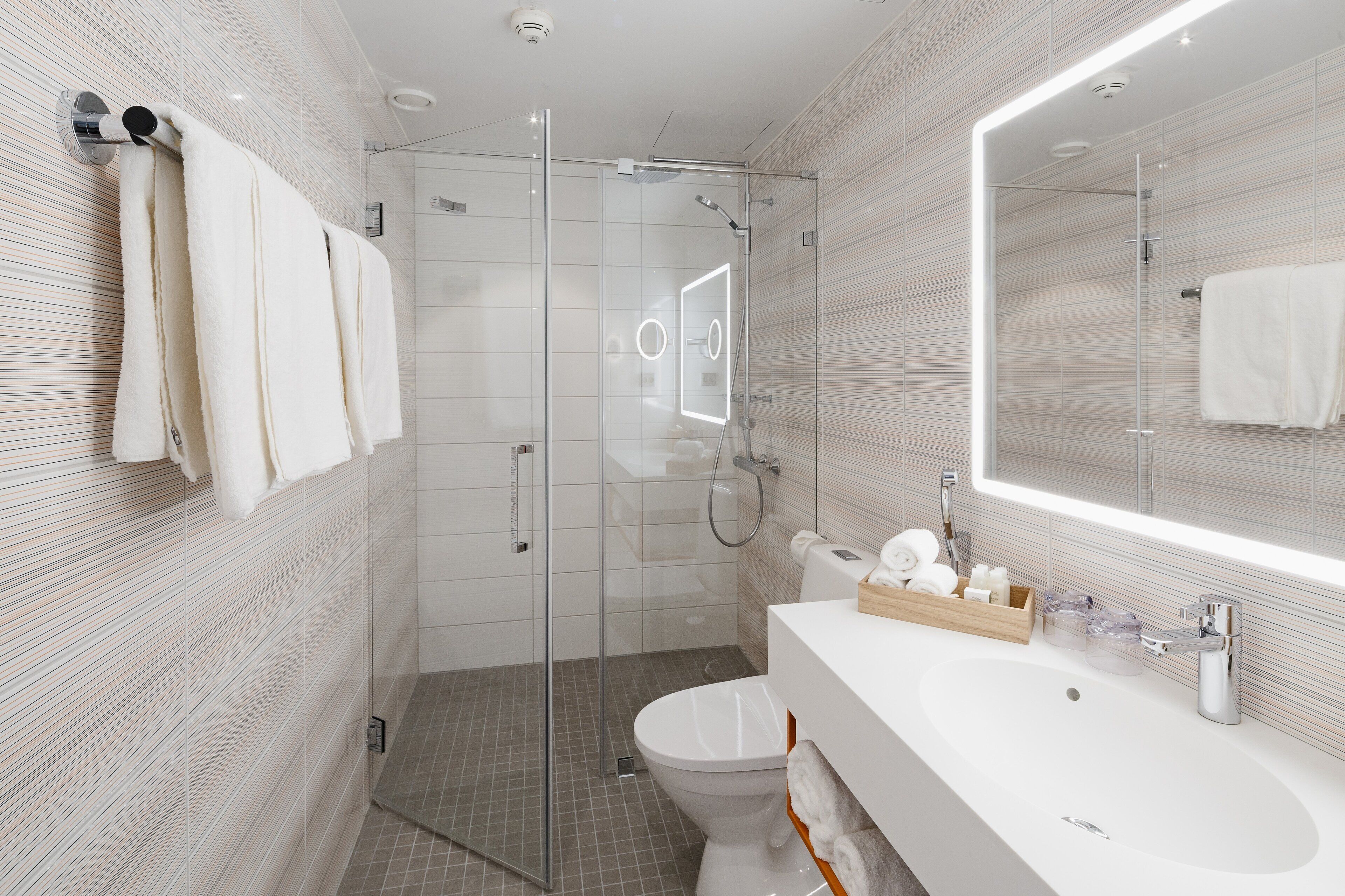 Un bagno moderno con doccia vetrata, lavabo bianco con vassoio in legno e uno specchio grande.