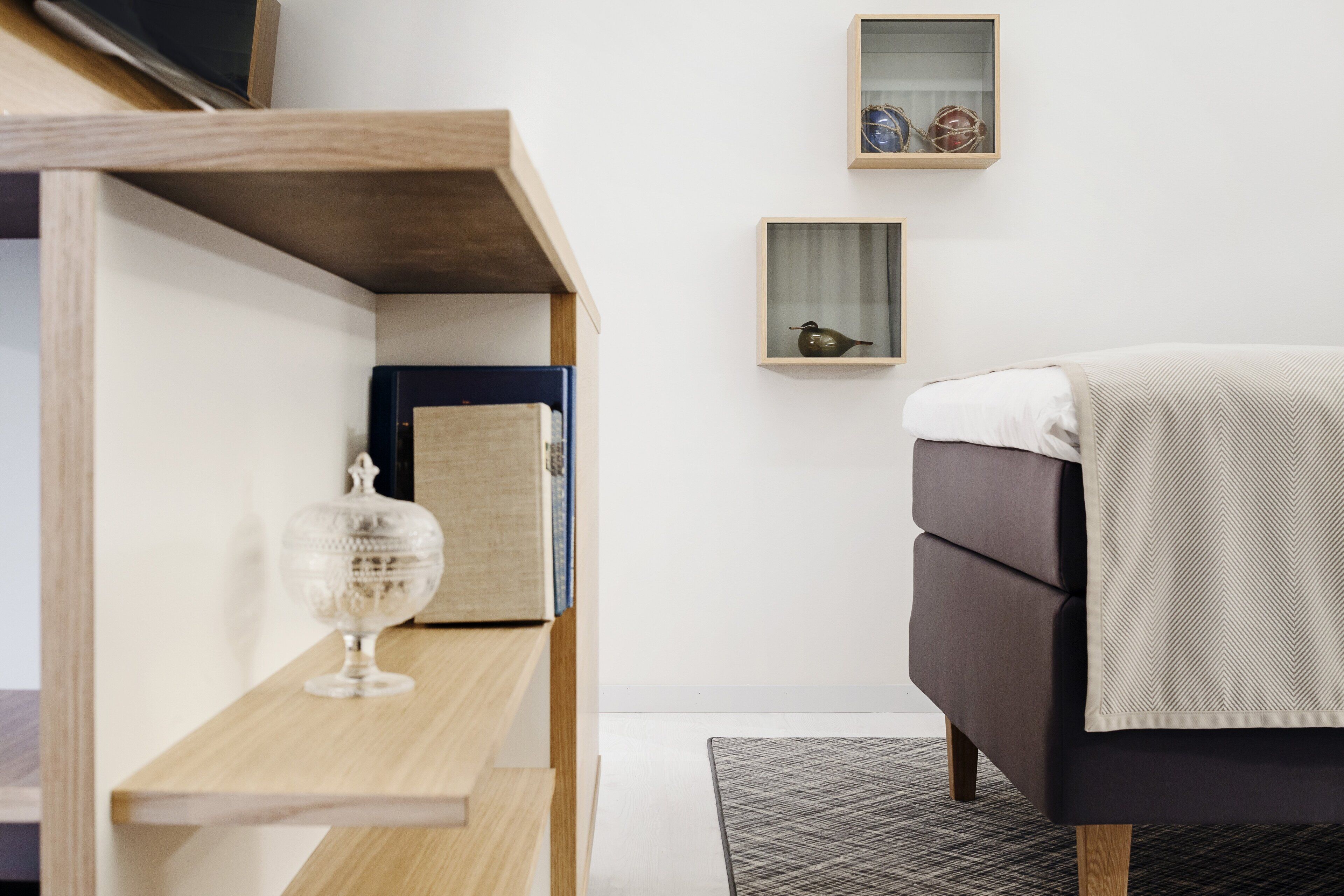 Une chambre à coucher moderne avec un lit, une étagère en bois ornée d’objets décoratifs et deux tableaux encadrés accrochés au mur.