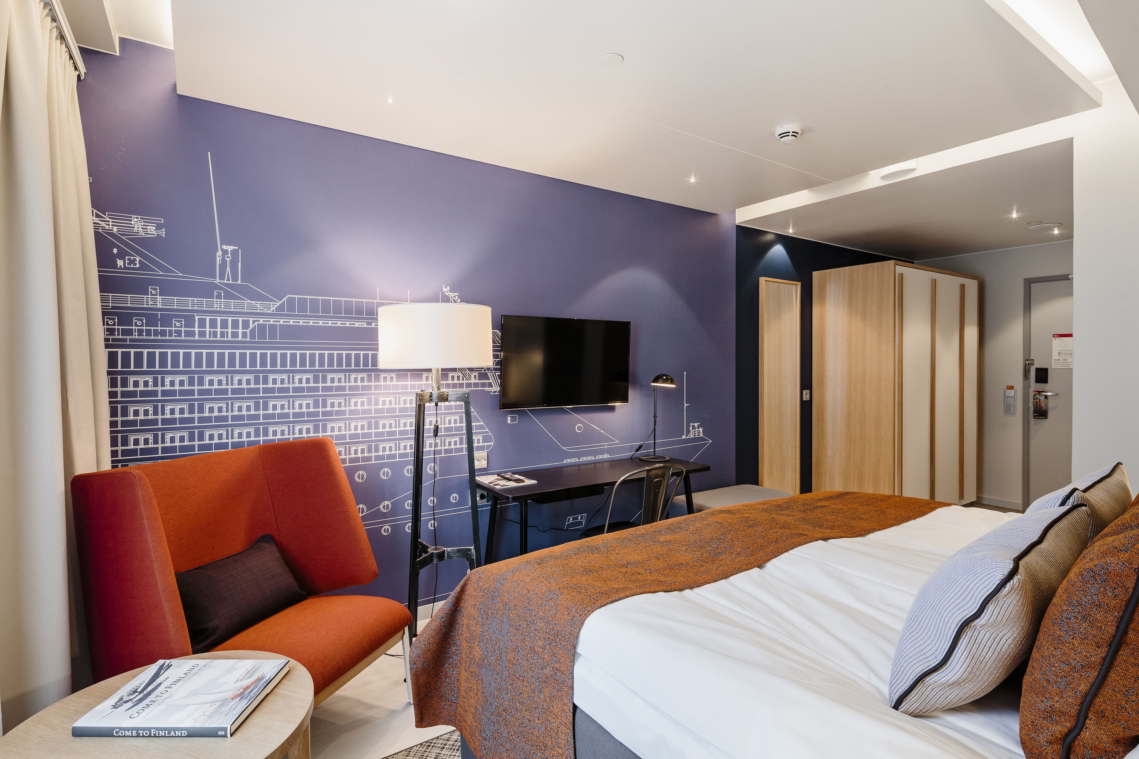 A hotel room with a bed, a desk, a chair, a TV, and a wardrobe.