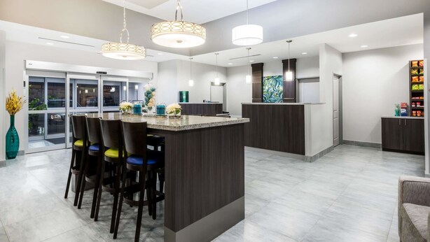 A modern kitchen with a central island, bar stools, pendant lighting, and a view of the outside.