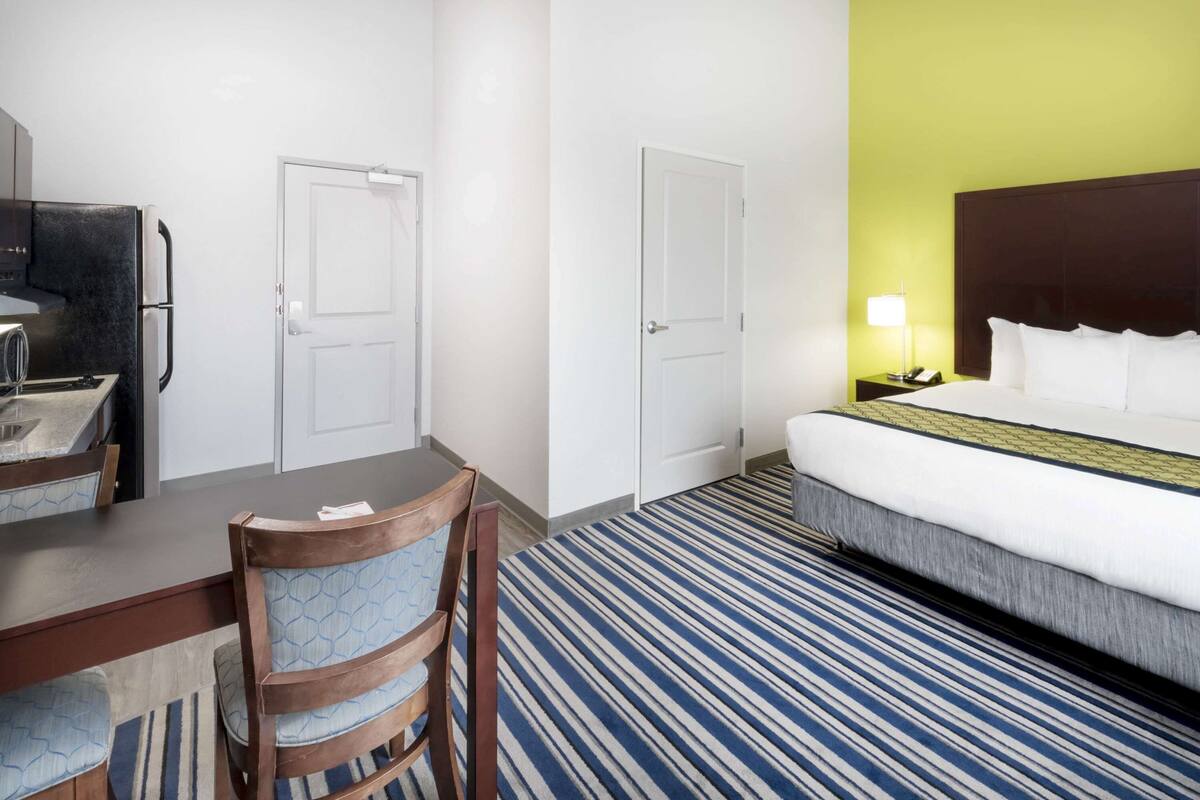 Hotellihuone, jossa on sänky, työpöytä tuolilla, jääkaappi ja kaksi ovea.
