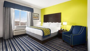 A hotel room with a bed, a chair, a nightstand, a lamp, and a window with curtains.