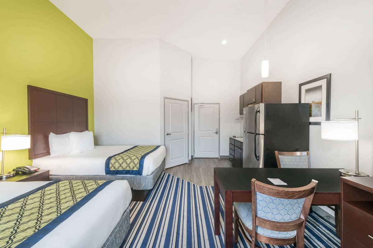 Hotellihuone, jossa on kaksi sänkyä, ruokapöytä, tuolit, jääkaappi, mikroaaltouuni, kahvinkeitin ja pieni kaappi.