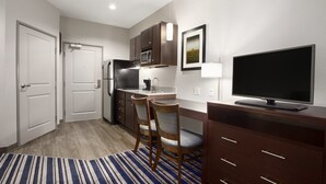 A compact kitchen with a refrigerator, microwave, and sink, a dining area with chairs, and a flat-screen TV on a wooden cabinet.