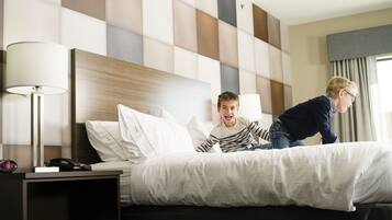 A hotel room with a modern design, featuring a large bed with white linens, a bedside table with a lamp, and a headboard with a geometric pattern.