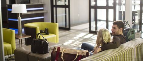 A modern hotel lobby with a reception desk, seating area, and a large window.