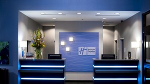 Un área de recepción de diseño moderno, con una mesa de recepción, un cartel de Holiday Inn Express y un jarrón decorativo con flores.