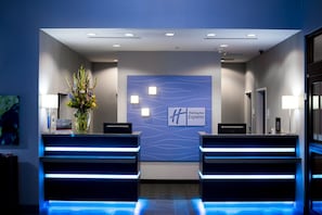 A reception area with a modern design, featuring a reception desk, a wall-mounted sign for Holiday Inn Express, and a decorative vase with flowers.