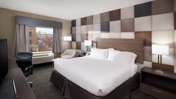 Habitación de hotel con una cama grande, un escritorio, una silla, un televisor, un calentador y una ventana con cortinas.