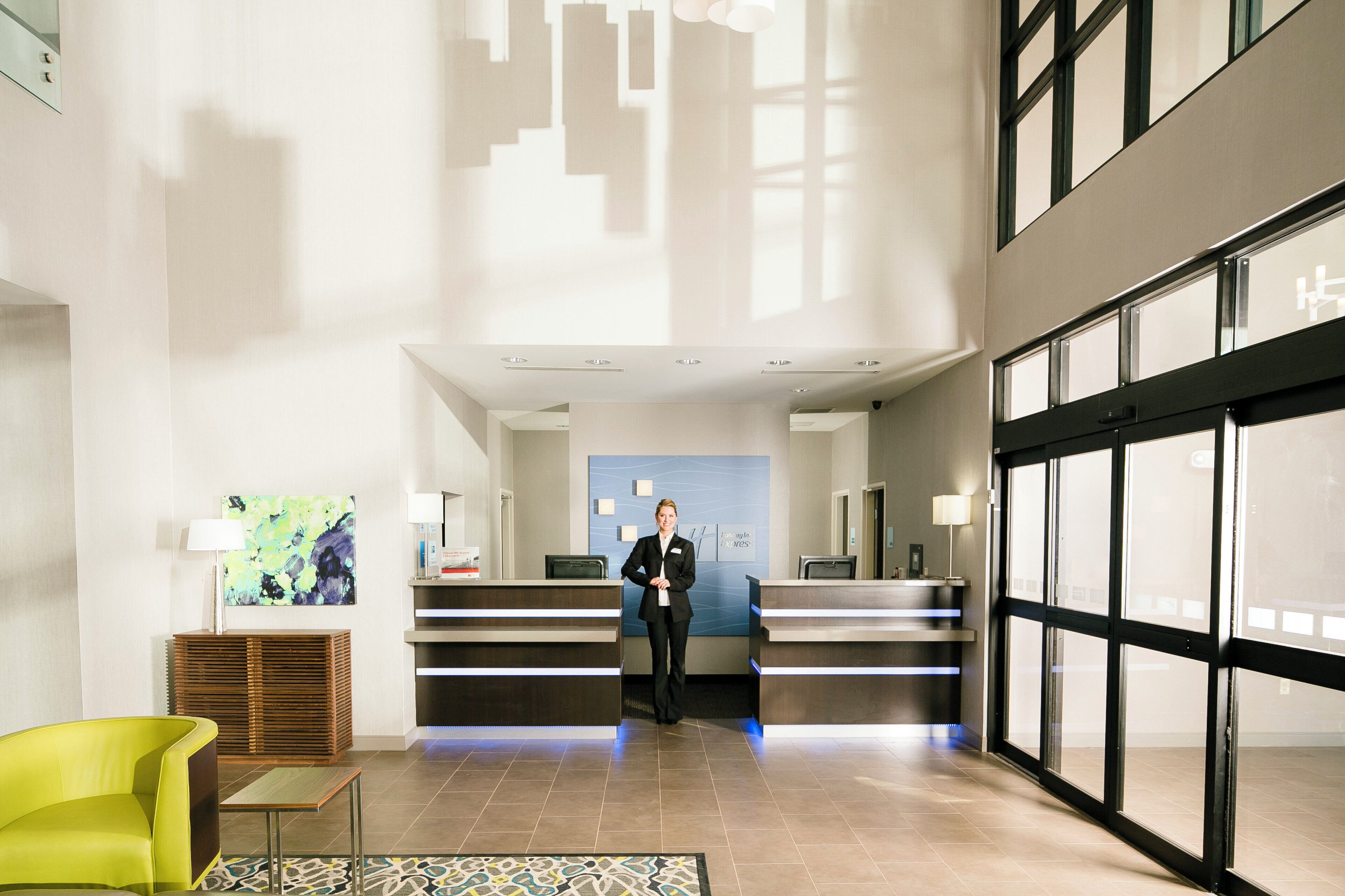 A hotel lobby with a reception desk, a receptionist, and a large window.