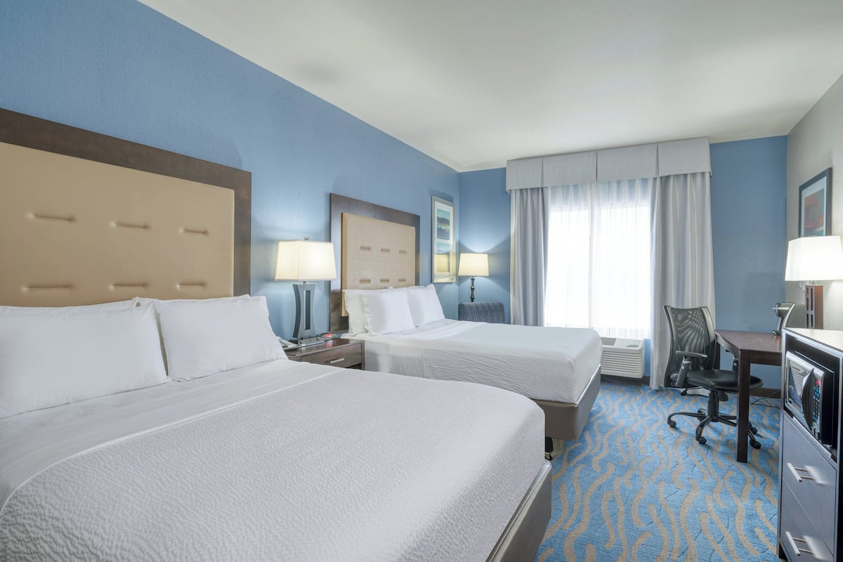 A hotel room with two beds, a desk, a chair, a TV, and a window with curtains.