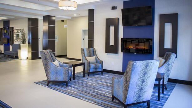 Un hall d’entrée moderne avec des fauteuils à motifs, une cheminée et un grand téléviseur mural.
