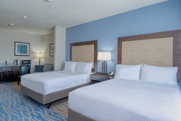 A hotel room with two beds, a desk, a chair, a lamp, and a painting on the wall.