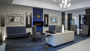 Un hall d’entrée moderne avec un tapis bleu à motifs, un canapé blanc, des fauteuils à motifs et un miroir décoratif.