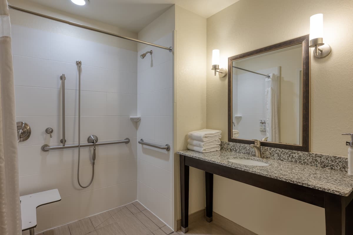 A bathroom with a shower, grab bars, a sink with a mirror, and a towel rack.