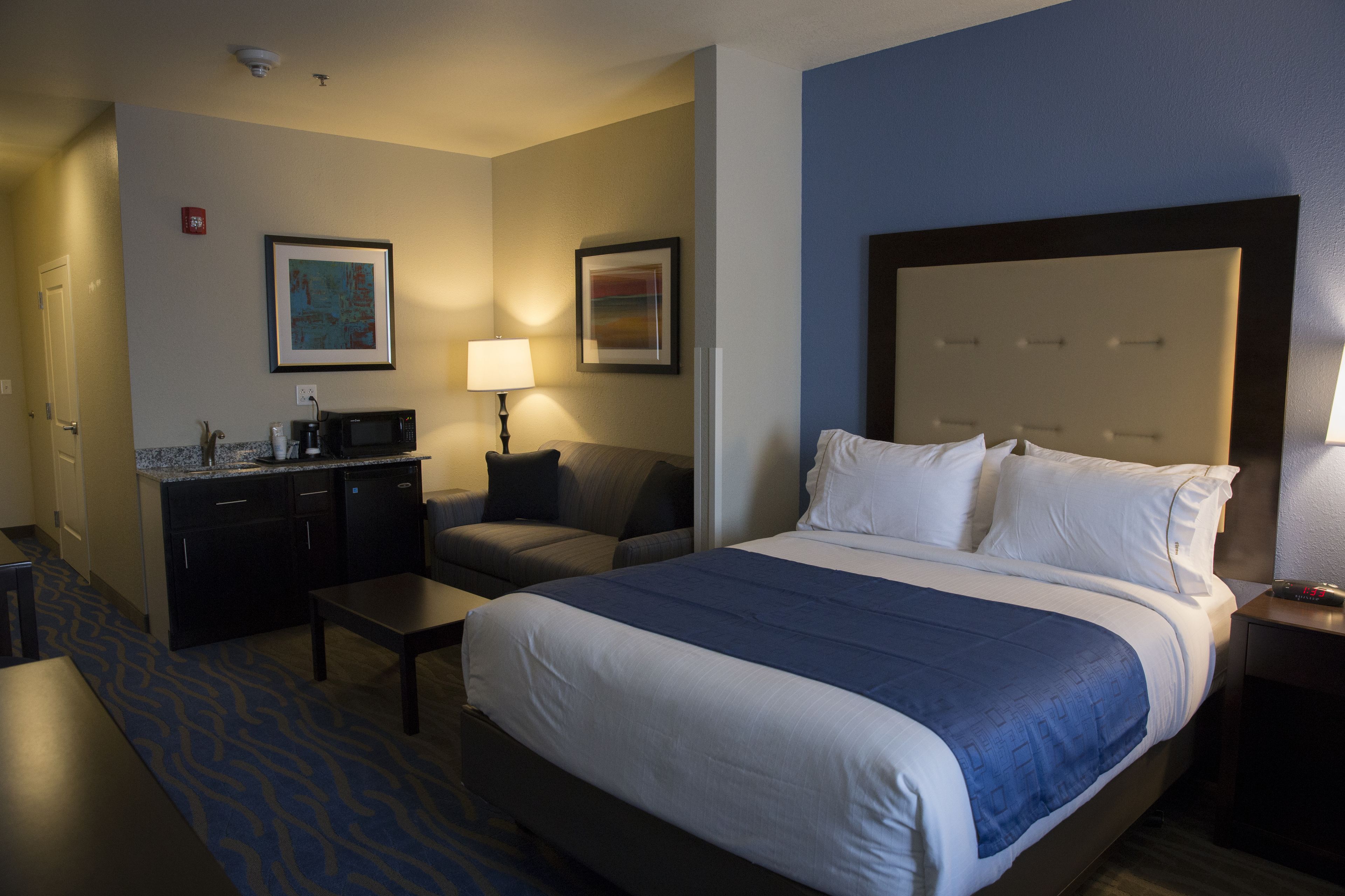 Habitación de hotel con cama, escritorio, silla, mesita, microondas y cafetera.
