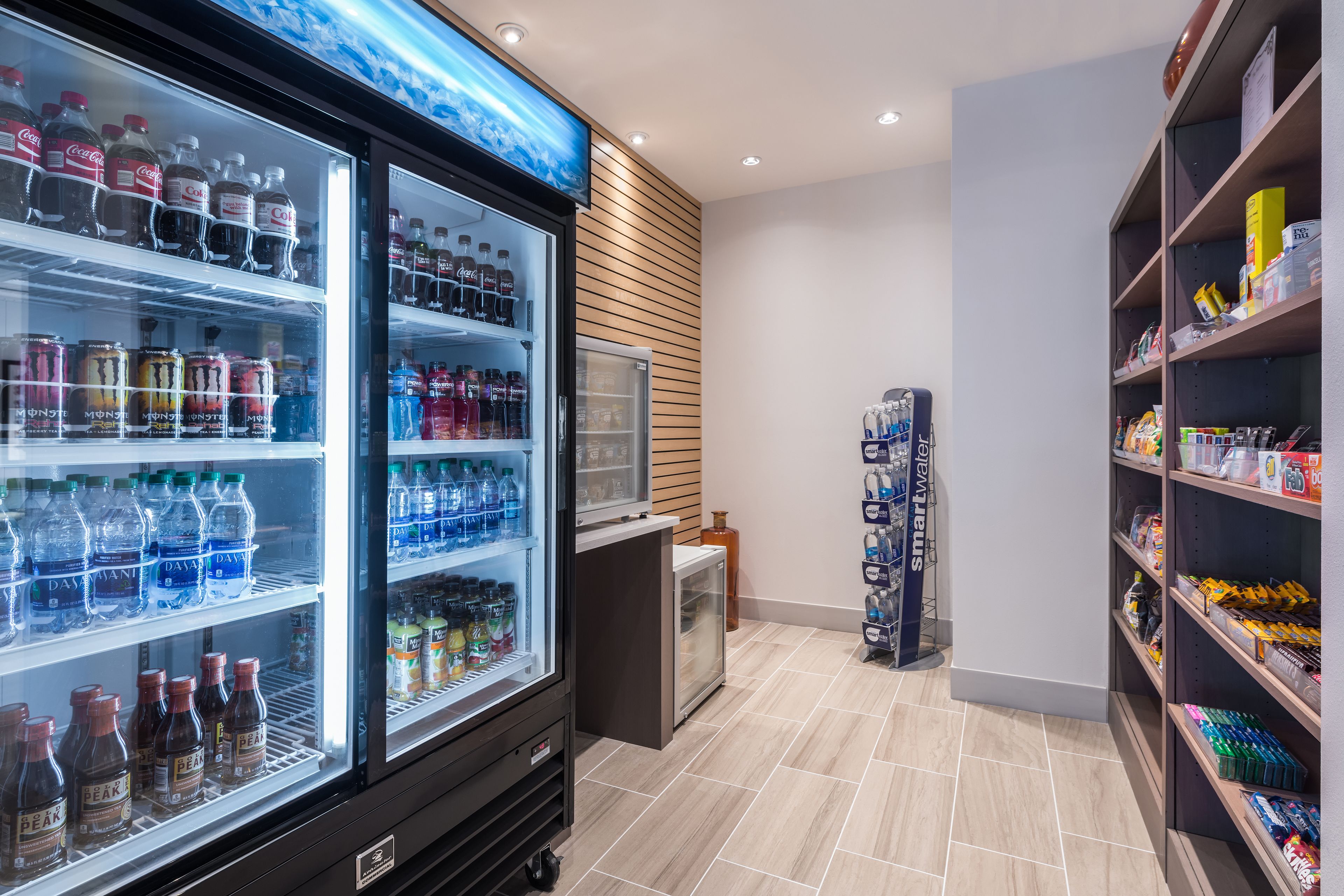 A beverage refrigerator stocked with various drinks, a small refrigerator, and shelves with snacks and bottled water.