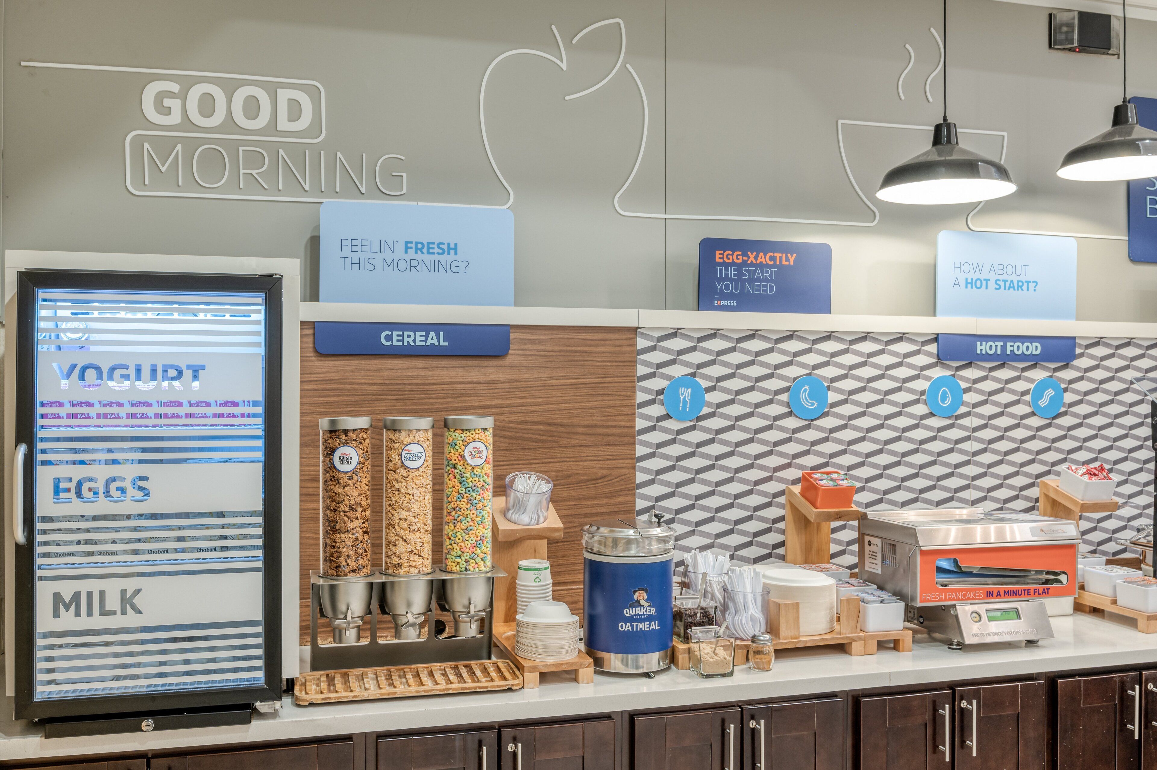 A breakfast station with a yogurt dispenser, cereal, eggs, milk, and a hot food station.