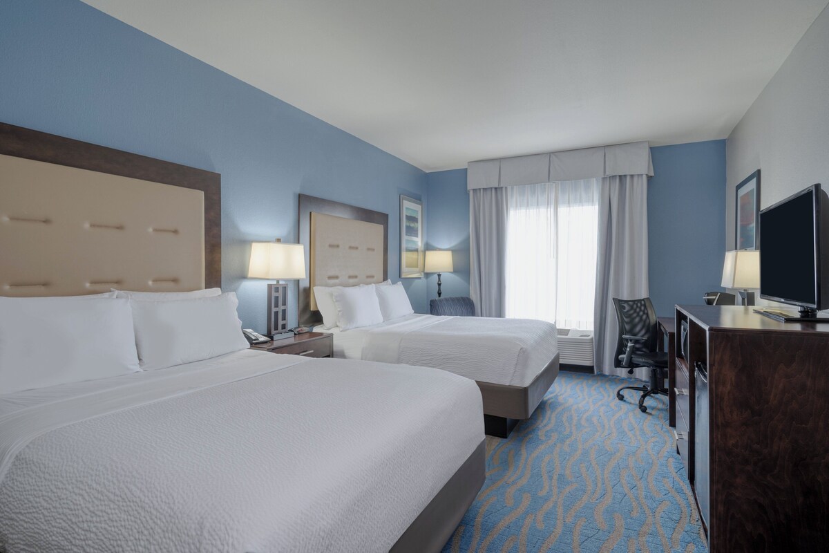 A hotel room with two beds, a desk, a chair, a television, and a window with curtains.