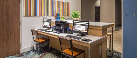 A modern office space with a desk, two chairs, two monitors, a printer, and a potted plant.