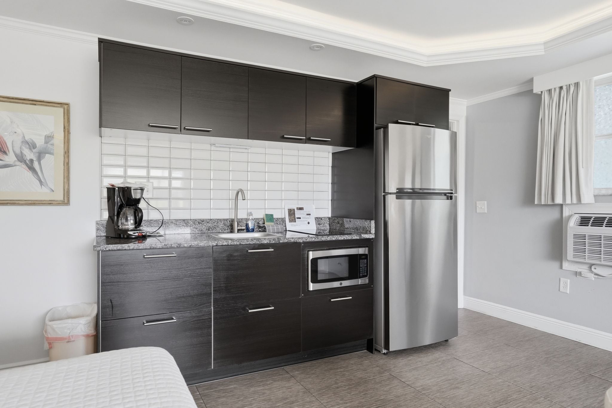 Una cocina compacta con armarios oscuros, un refrigerador de acero inoxidable, un horno empotrado y un microondas.