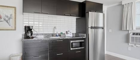 Una cocina compacta con armarios oscuros, un refrigerador de acero inoxidable, un horno empotrado y un microondas.
