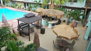 Zona de piscina en la azotea con estación de barbacoa, mobiliario exterior y sombrillas de paja.