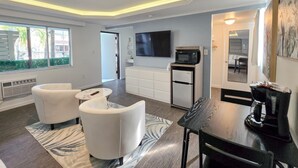 Una sala de estar moderna con comedor, un televisor de pantalla plana montado en la pared, microondas empotrado y refrigerador.