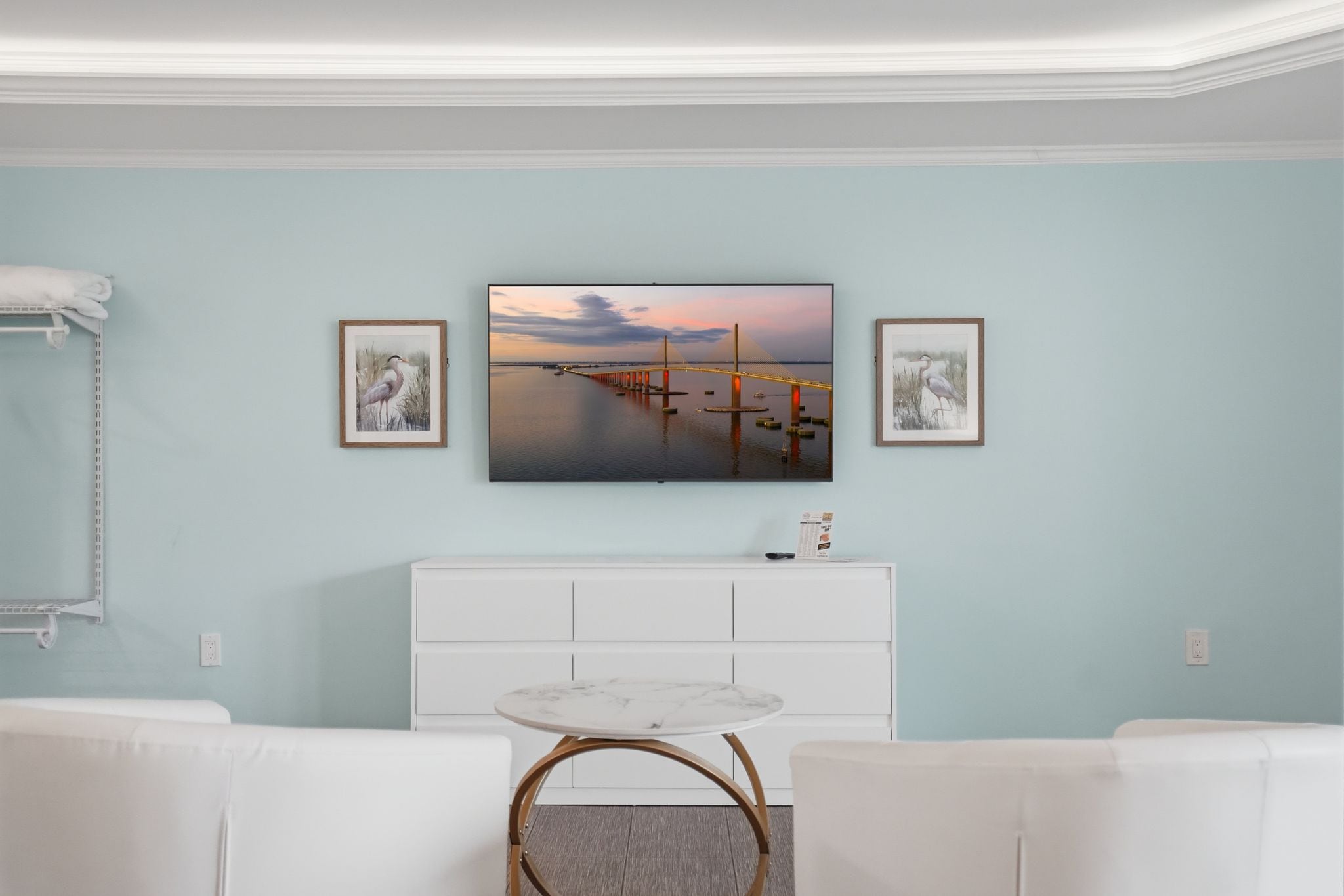A modern living room with a white sofa set, a marble coffee table, and a large framed picture of a bridge over water.