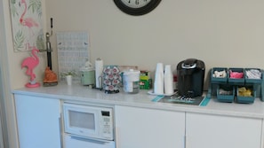 Una encimera de cocina con cafetera, tazas, microondas y diversos utensilios.