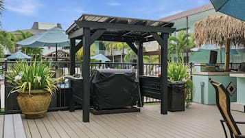 Un patio exterior con zona de parrilla cubierta, plantas en macetas y sombrillas.