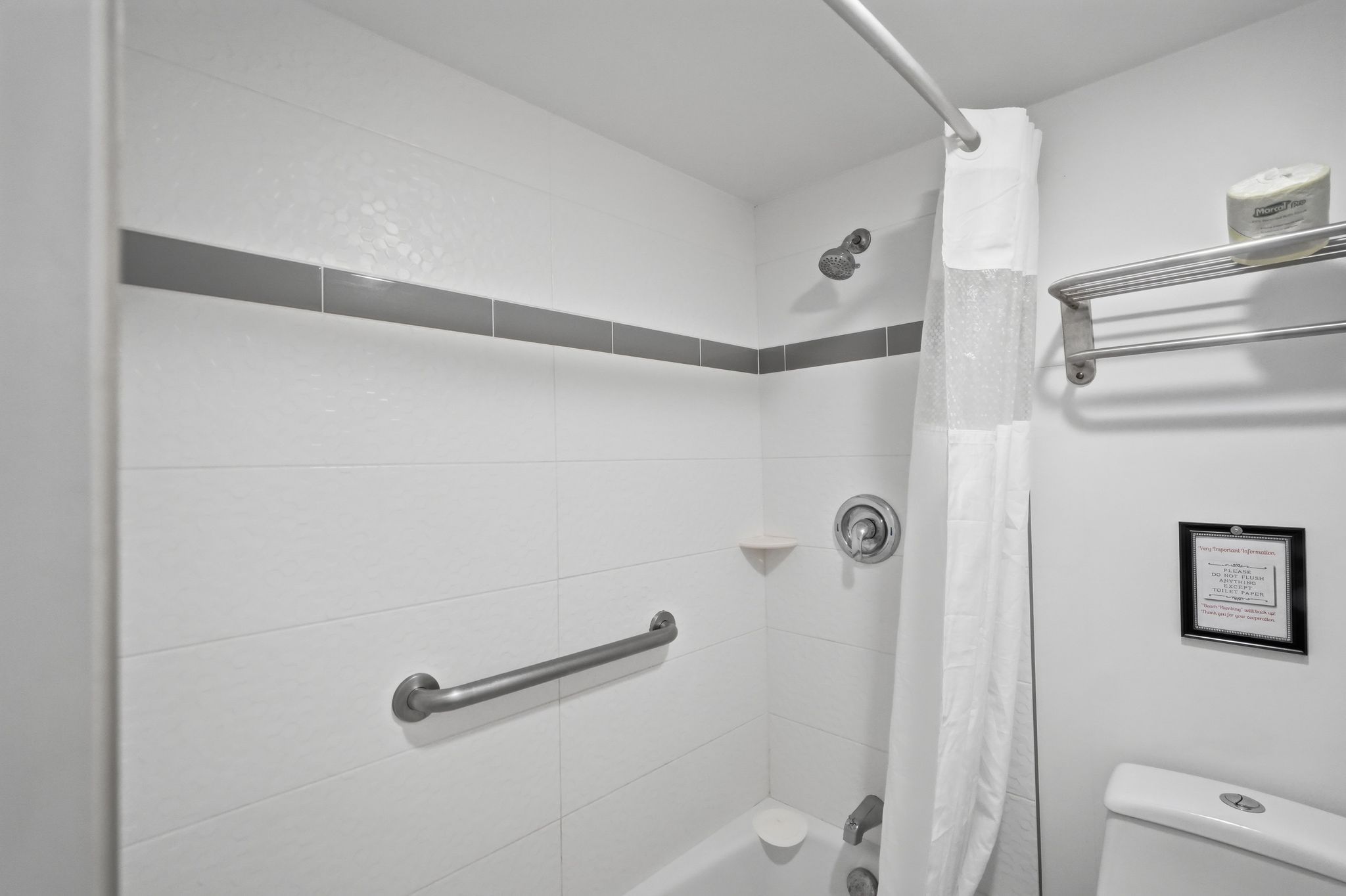 Une salle de bain avec des carreaux blancs, un rideau de douche, une barre d’appui, un porte-serviettes et un panneau sur le mur.