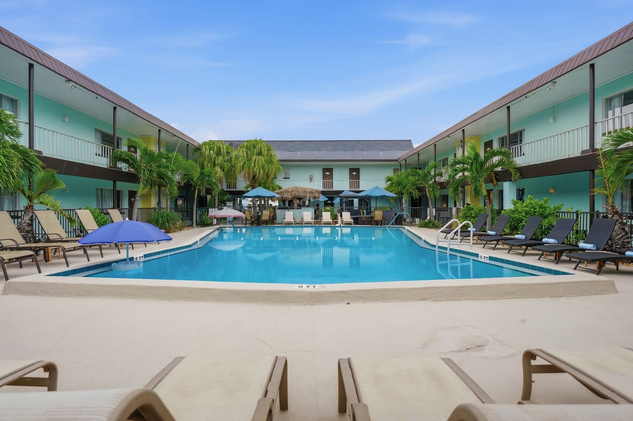 A swimming pool with lounge chairs and umbrellas, surrounded by a building with balconies.