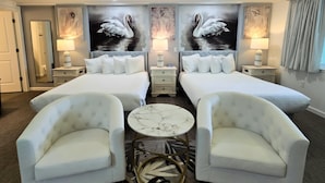 Habitación de hotel con dos camas, una zona de estar con sillones, una mesa de centro de mármol y cuadros de cisnes en las paredes.