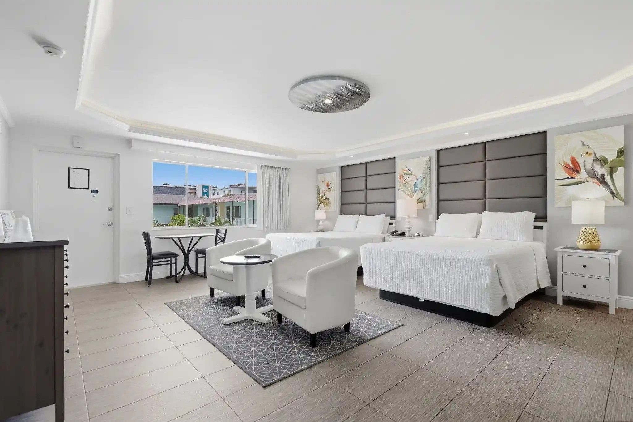 Quarto de hotel com cama, duas mesas de cabeceira, escrivaninha e cadeira, além de vista para edifícios.