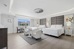 Une chambre d’hôtel comprenant un lit, deux tables de chevet, un bureau avec une chaise et une vue sur les bâtiments environnants.